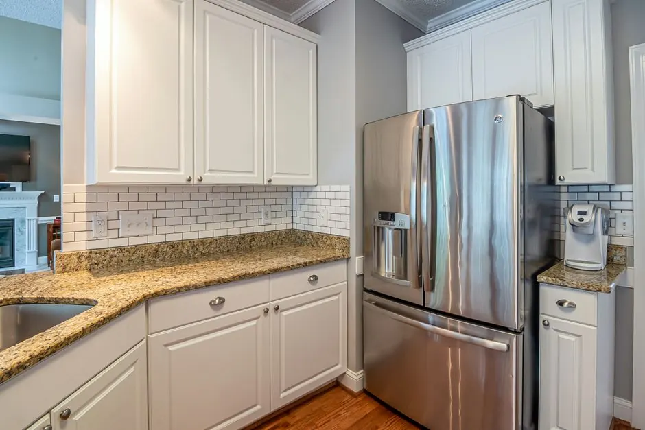 Bright modern kitchen with granite countertops, stainless steel appliances, and white cabinetry.